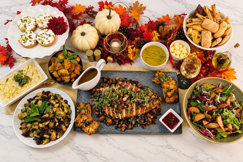 The Marigolds & Onions Thanksgiving spread: sliced turkey, Brussels sprouts, pear salad, squash soup, dressing and pumpkin tarts among autumn leaves